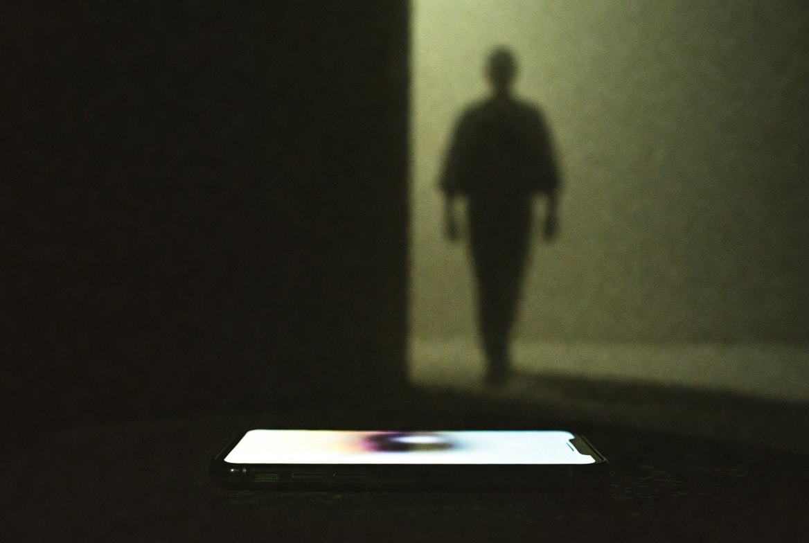 silhouette of person walking into darkness with a glowing phone left behind on a dark surface - visual metaphor for social media viewers who disappear without leaving contact